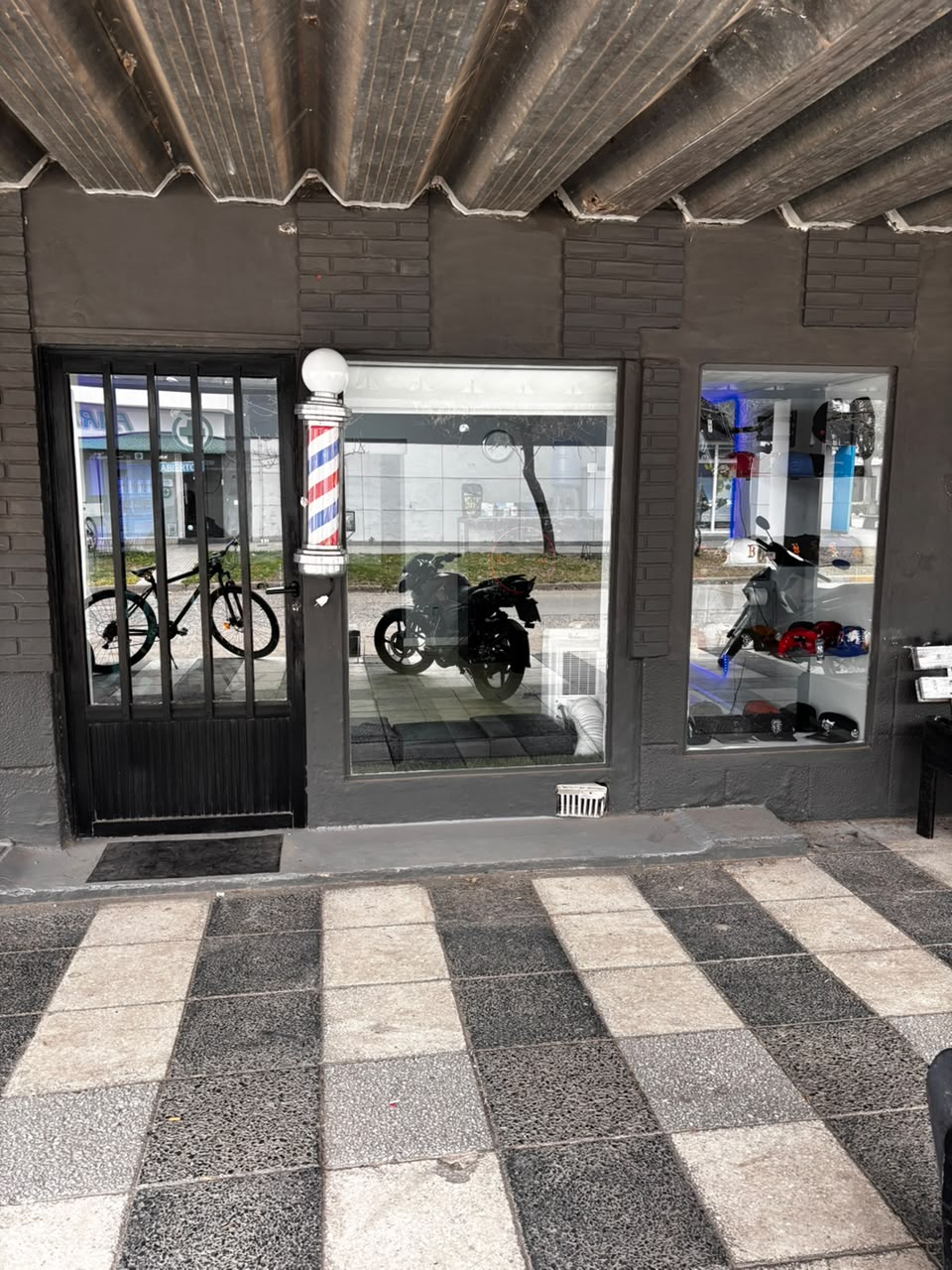 Fachada de Navajas de día, con el poste de barbería y la vidriera de gorras